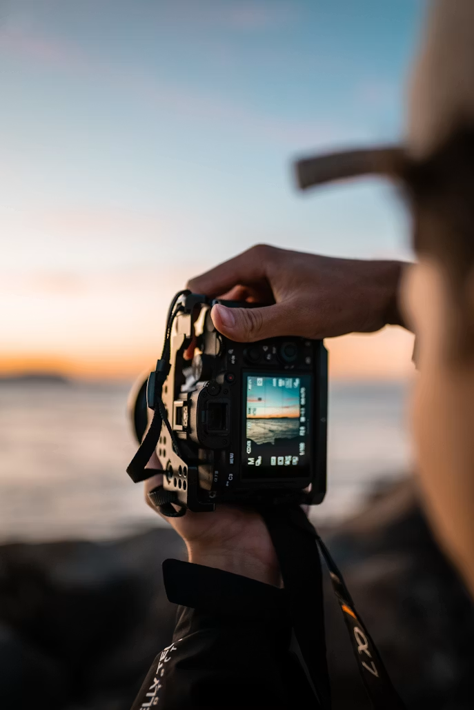 Fotograf hält Kamera im Sonnenuntergang am Meer